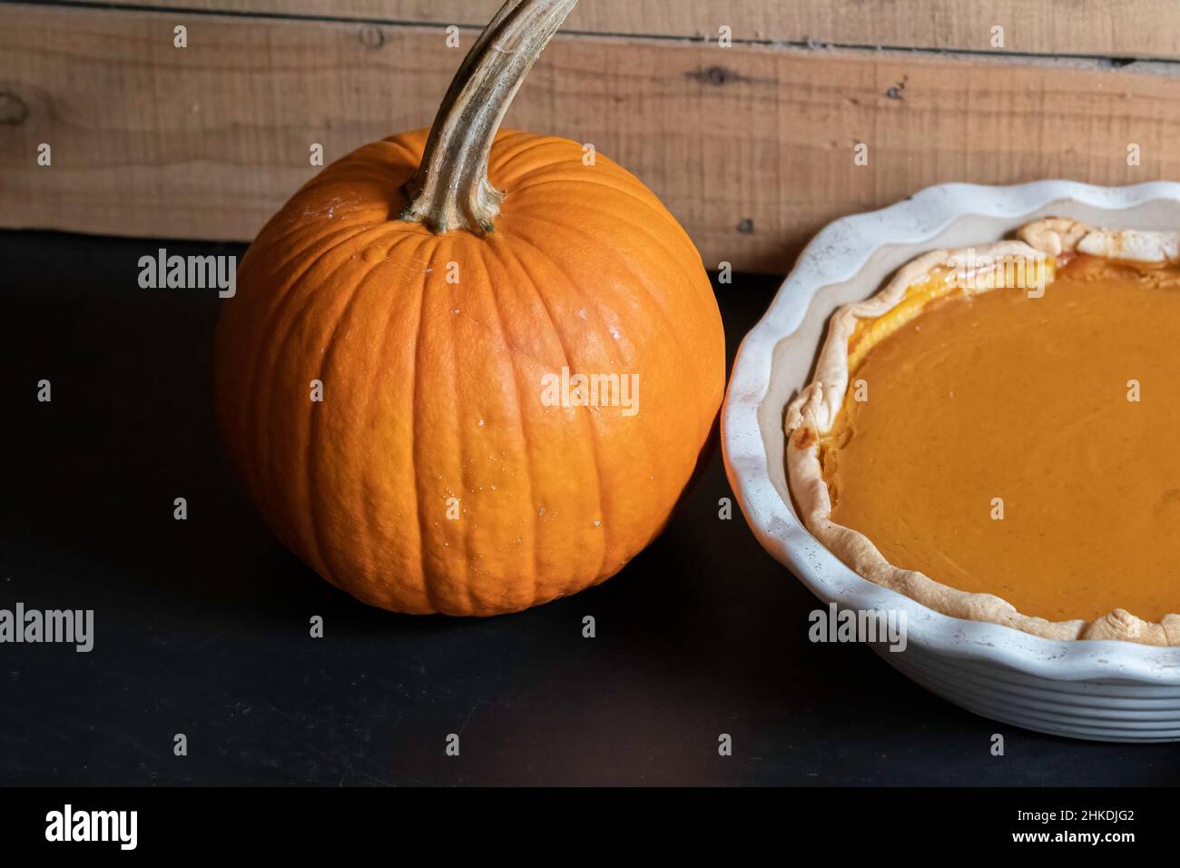 Hintergrund eines ganzen Pie-Kürbisses neben einem gebackenen Kürbiskuchen mit negativem Abstand. Stockfoto