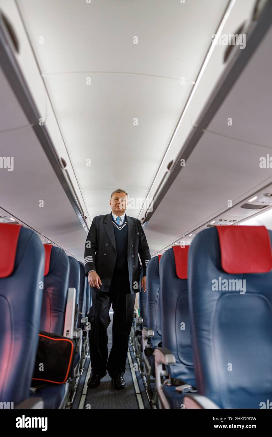 Männlicher Flugzeugpilot, der den Passagiersalon des Flugzeugs hinuntergeht Stockfoto