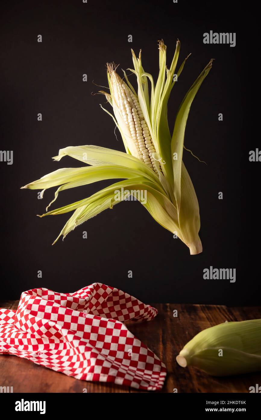 Kreatives Bild von rohem weißem Mais auf der Kohle schweben auf Holz rustikalen Tisch. Stockfoto