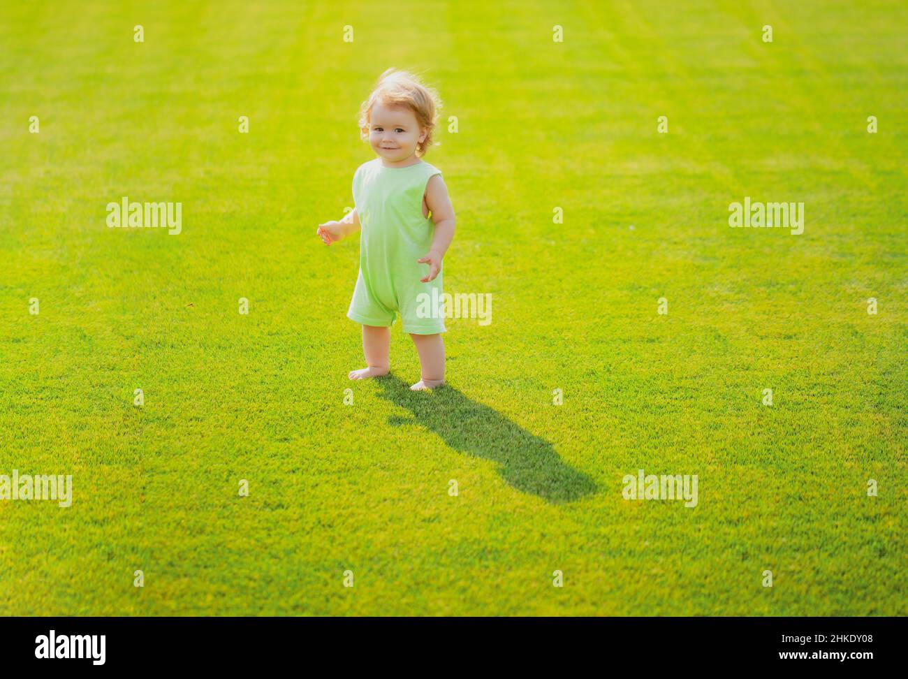 Baby steht barfuß auf dem grünen Rasen. Kleiner Junge, der im Sommerpark spielt. Glückliche Kindheit und Kinderpflege. Stockfoto