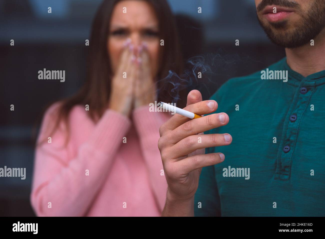 Passivrauchen. Mann raucht Zigarette in der Nähe einer Frau, die ihr Gesicht vor Zigarettenrauch bedeckt. Stockfoto