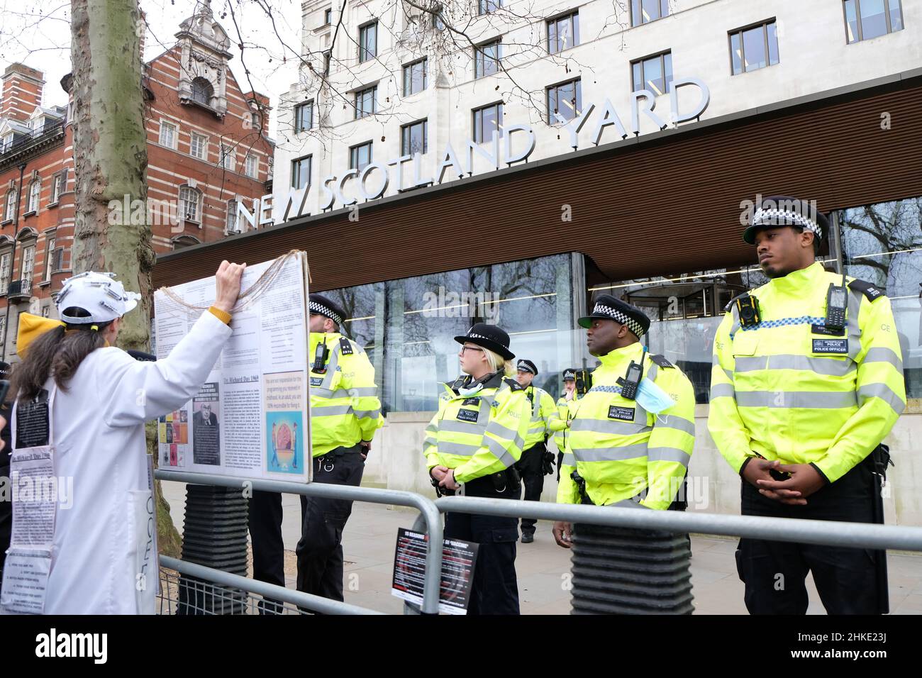 London, Großbritannien. Die Met-Polizisten stehen vor dem New Scotland Yard, als ein Protestler mit einem Plakat an Metallbarrieren steht. Stockfoto