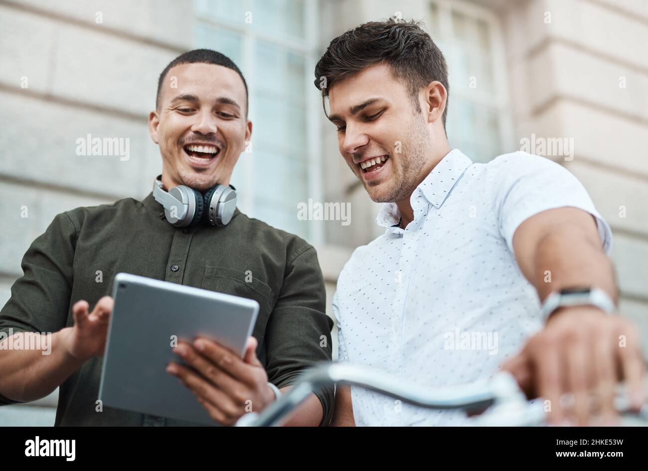 Wie Millennials Dinge ermöglichen. Aufnahme von zwei jungen Geschäftsleuten, die zusammen ein digitales Tablet benutzen, während sie in der Stadt mit dem Fahrrad fahren. Stockfoto