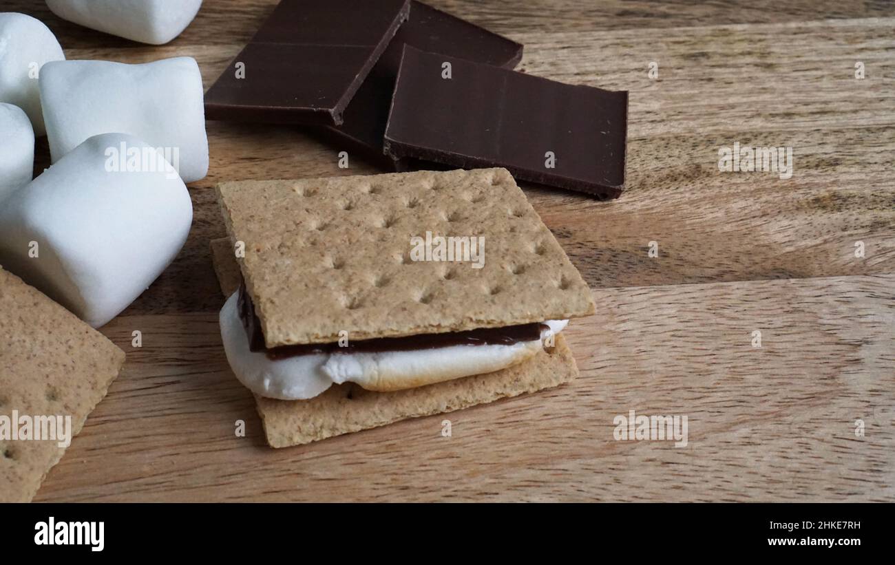 Making s'mores - Schokolade, Marschwalben und graham Cracker auf einem hölzernen Hintergrund. Stockfoto