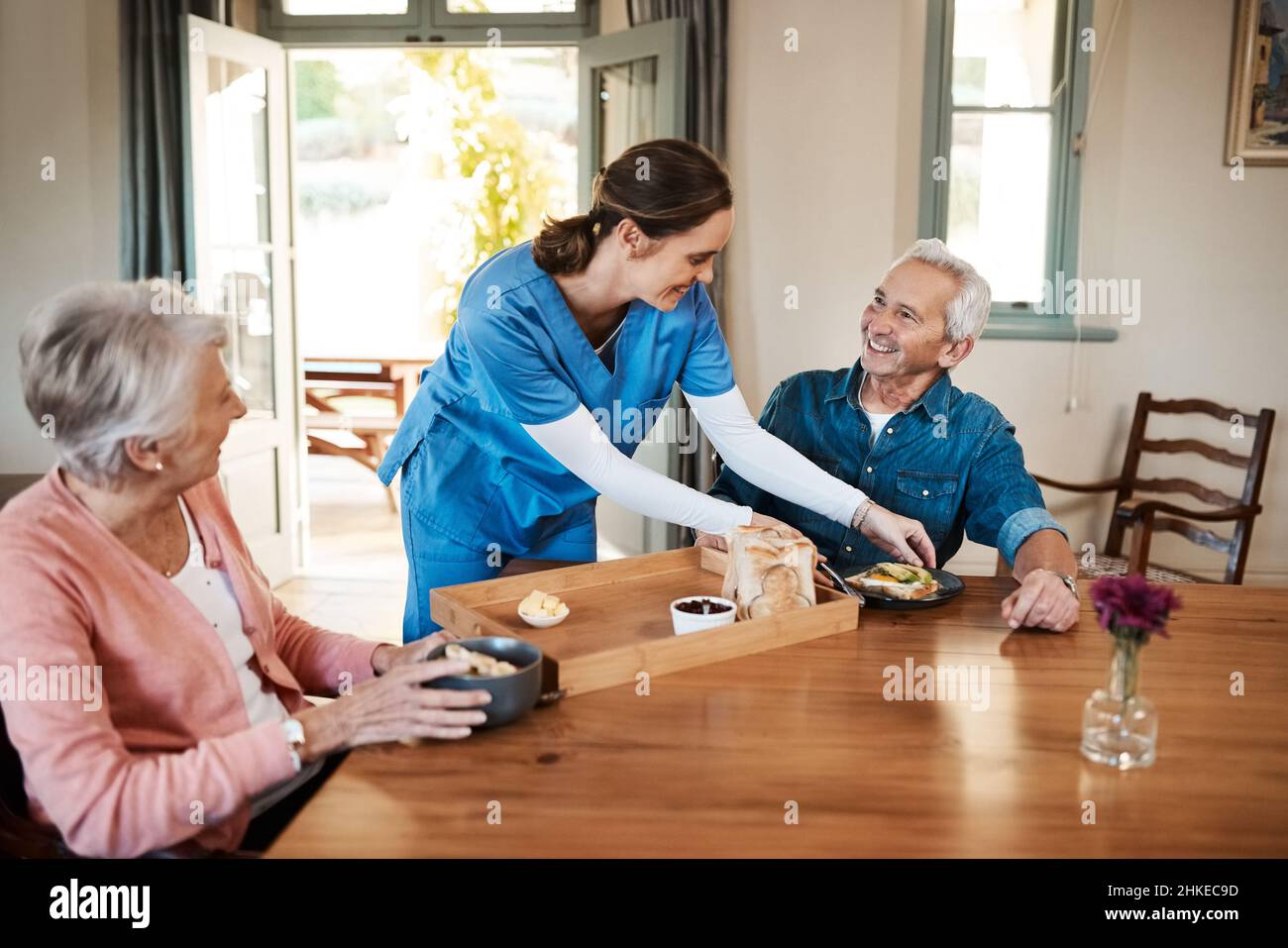 Es ist sogar noch besser als ein Restaurant. Aufnahme einer jungen Krankenschwester, die während des Frühstücks in einem Pflegeheim ein Seniorenpaar aufgesucht hat. Stockfoto