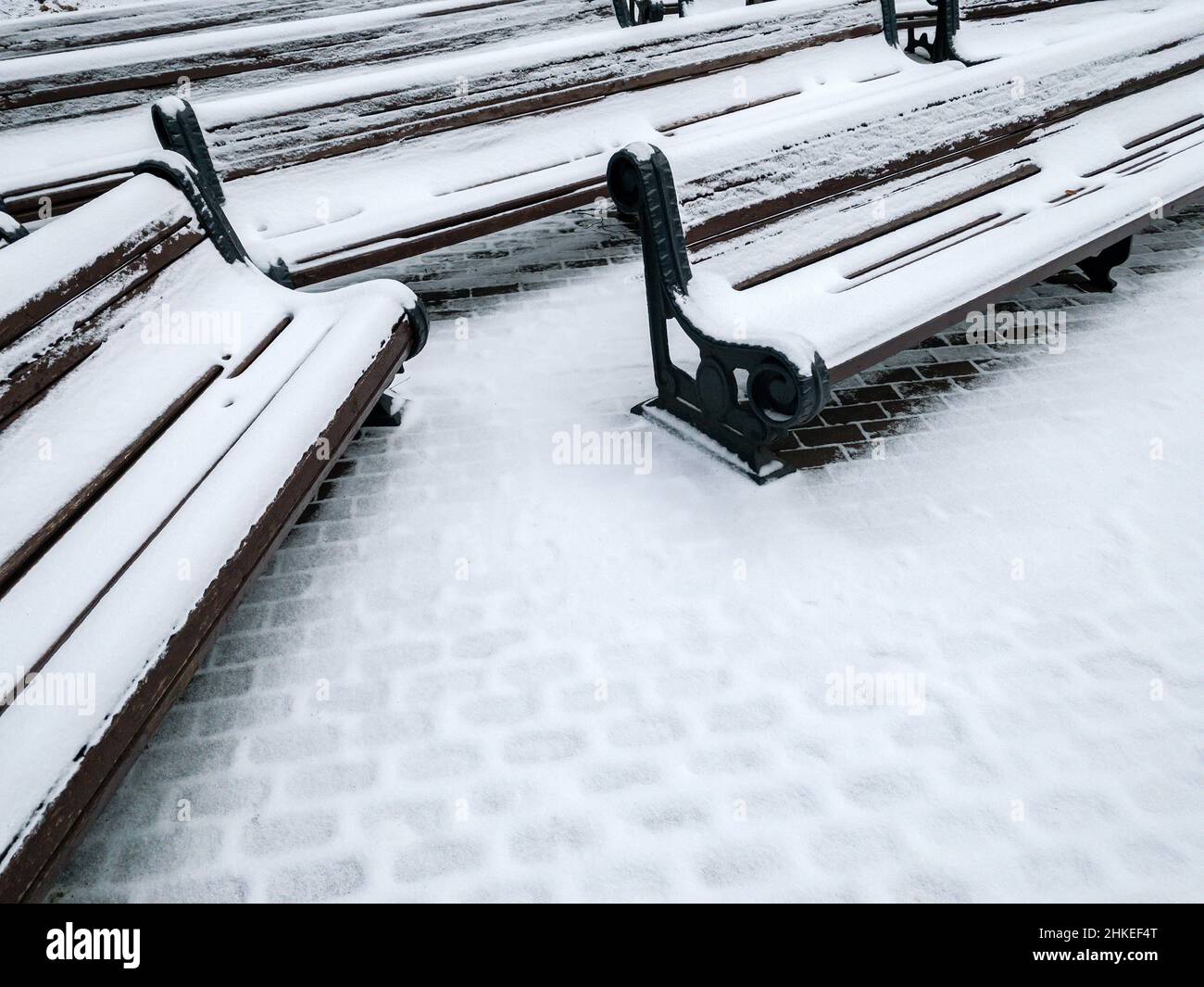 Schnee auf Bänken und Wanderwegen im Park. Kalter Wintertag. Stockfoto