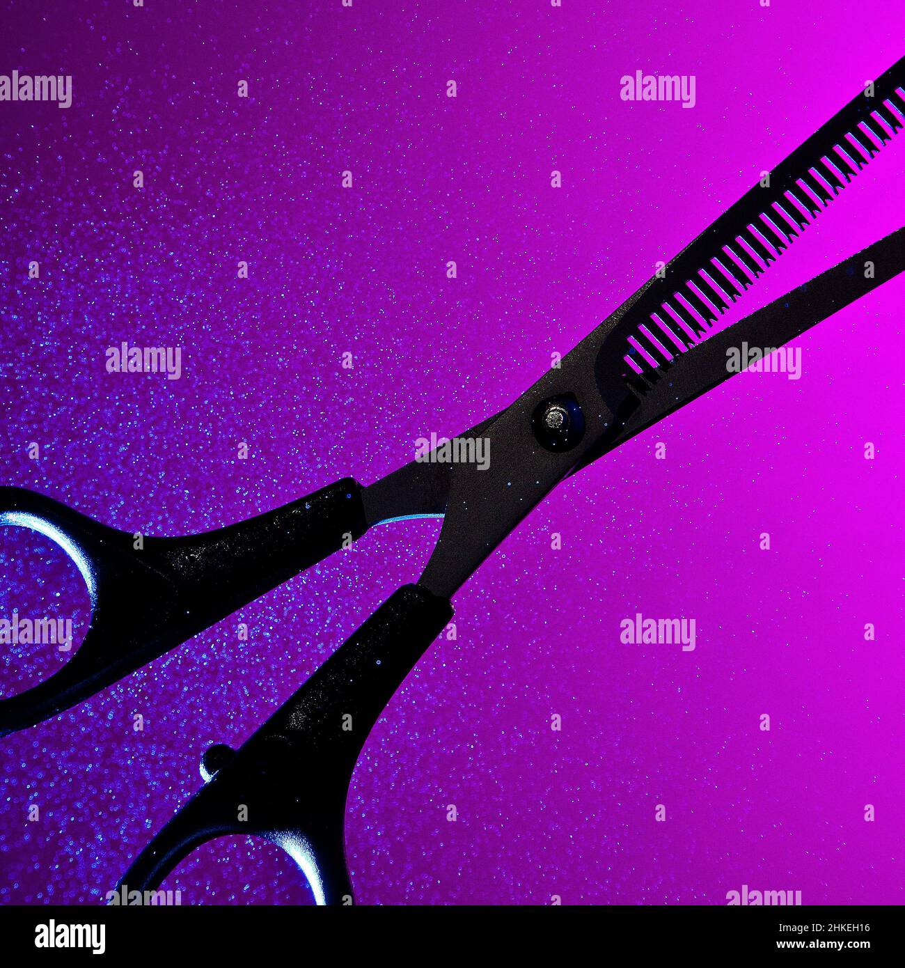 Eine abstrakte konzeptuelle kunstvolle Silhouette aus dünner werdendem Scheren, die vor einem sattvioletten und rosa Hintergrund mit einem glühenden Nebelspray beleuchtet wird Stockfoto
