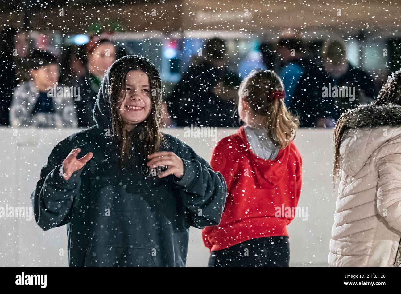 Prattville, Alabama, USA - 23. Dezember 2021: Ein Mädchen lächelt und lacht, als künstlicher Schnee auf sie auf der Eislaufbahn im historischen Downtow fällt Stockfoto