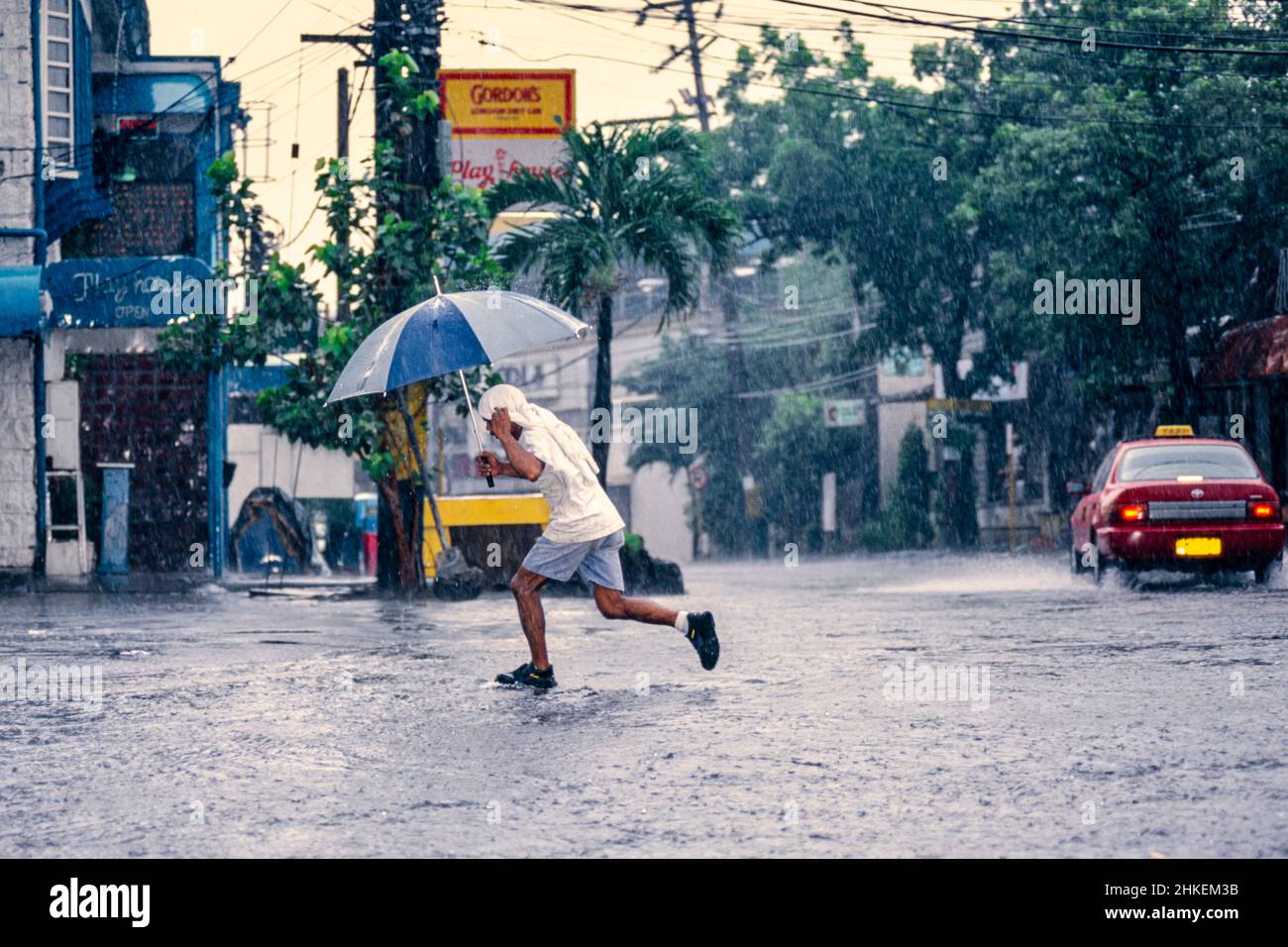 Kind, das während eines starken Regensturms im Zentrum von Manila, Philippinen, mit Regenschirm über die Straße läuft Stockfoto