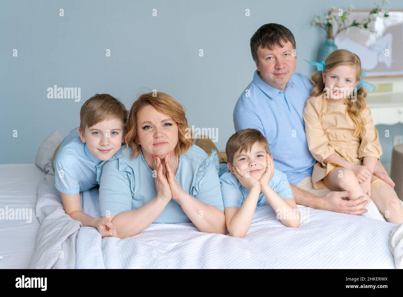Glückliche Familie, die auf ihrem Bett im Schlafzimmer die Kamera ansah. Kaukasische Eltern und Kinder liegen und haben Spaß zu Hause in ihrer Freizeit. Große freundliche Familie ruht sich im Urlaub aus. Söhne und süße Tochter Stockfoto