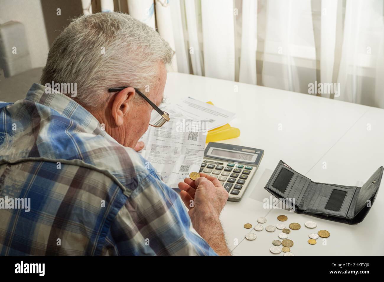 Älterer Mann, der am Tisch sitzt und die Finanzen berechnet. Alter Mann, der Rechnungen überprüft. Mann, der Münzen auf dem Tisch zählt. Pensionsberechnungskonzept Stockfoto