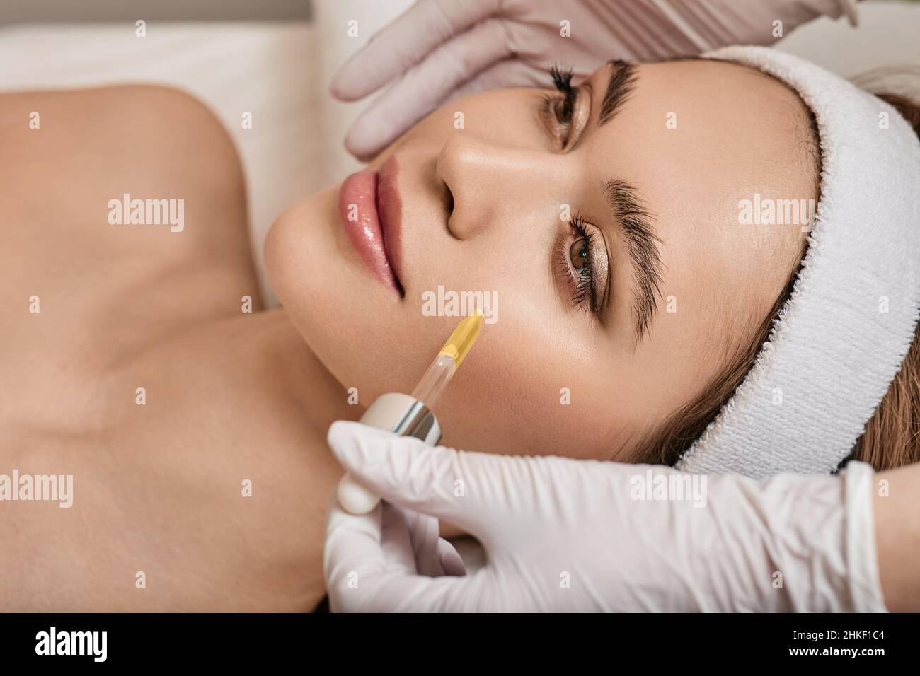 Gesichtshaut-Pflege mit Kosmetiköl und Serum. Schöne Frau, während die Kosmetikerin im Schönheitssalon Serum auf ihr Gesicht aufträgt Stockfoto