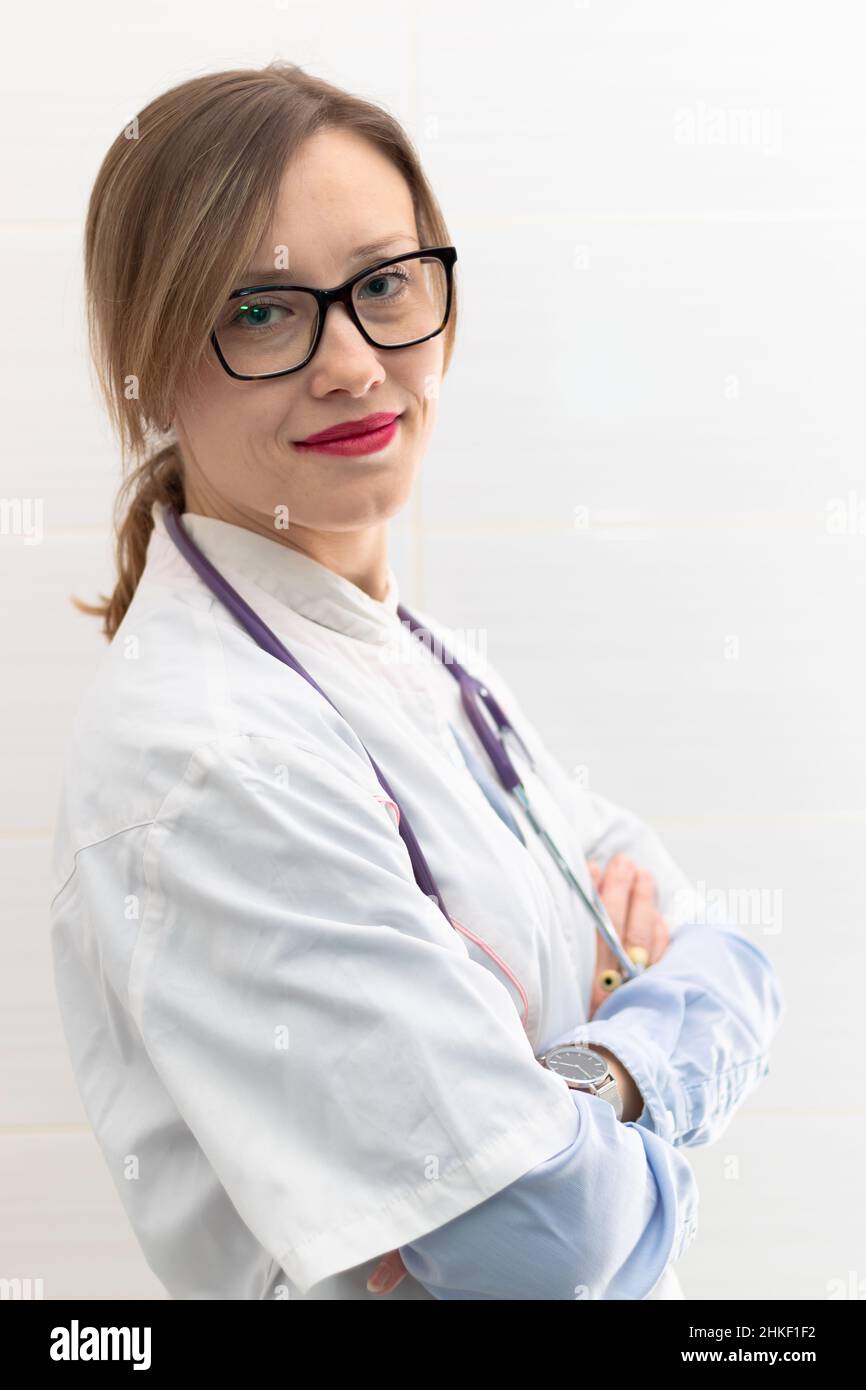 Schöne junge Ärztin in einem medizinischen Mantel und einer Brille mit Stethoskop in einem Krankenhaus auf weißem Hintergrund. Selektiver Fokus. Hochformat. Nahaufnahme Stockfoto