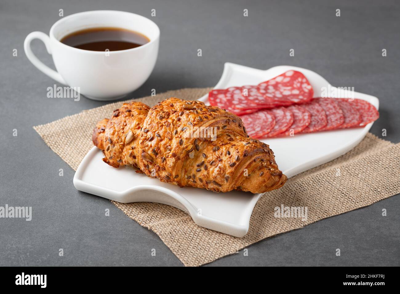 Frisches Croissant-Sandwich mit Wurst und Kaffee auf grauem Tisch Stockfoto