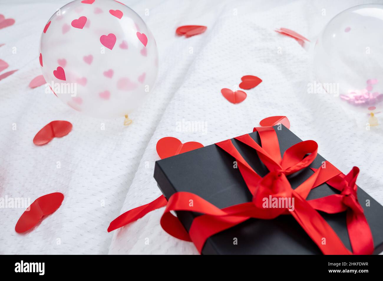 Geschenkbox verpackt und Postkarte mit einer roten schönen Schleife auf dem Bett dekoriert. Valentinstag, Geburtstagsgeschenk. Konzept für Hochzeitsreisende. Liebhaber Stockfoto