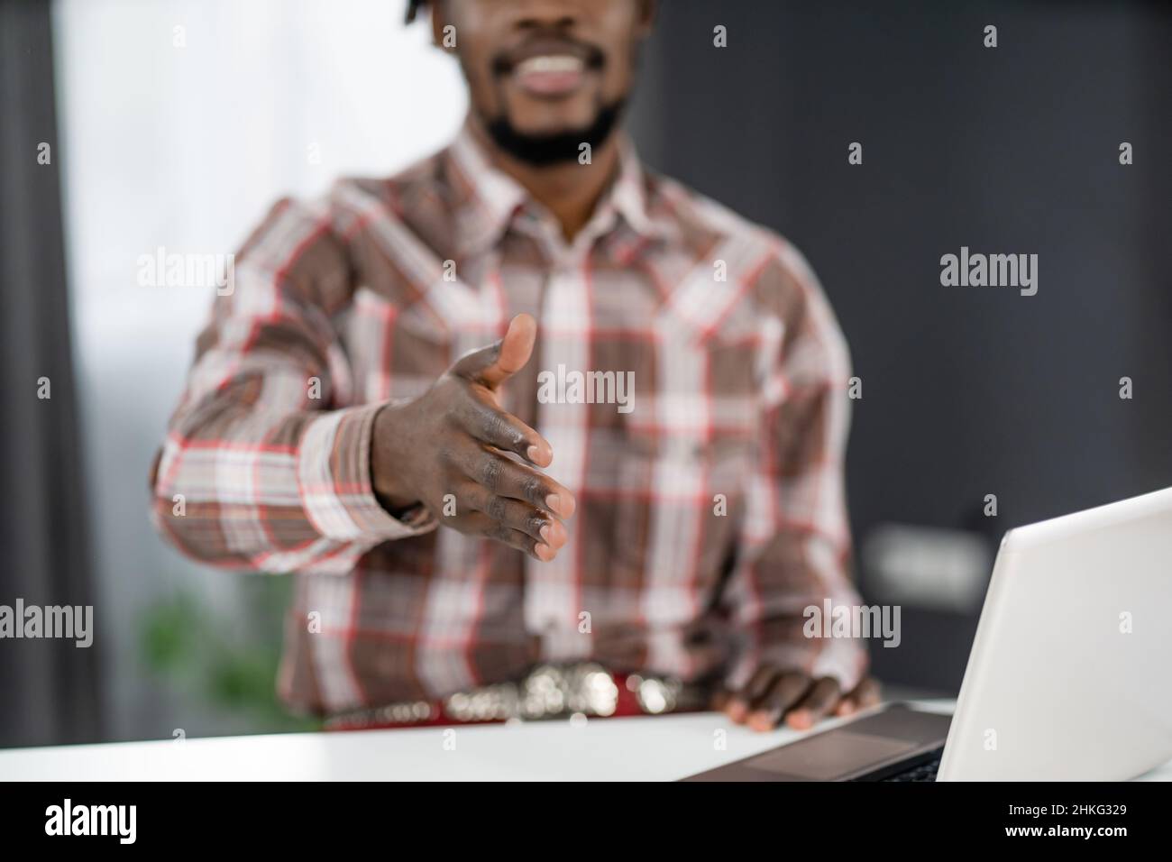 afroamerikanische Freiberuflerin, die mit einem Laptop im Büro sitzt und die Hand für einen Shake reicht. Junge Unternehmerin schüttelt einem Besucher, der im Büro sitzt, die Hand. Konzept für Bewerbungsgespräche. Stockfoto