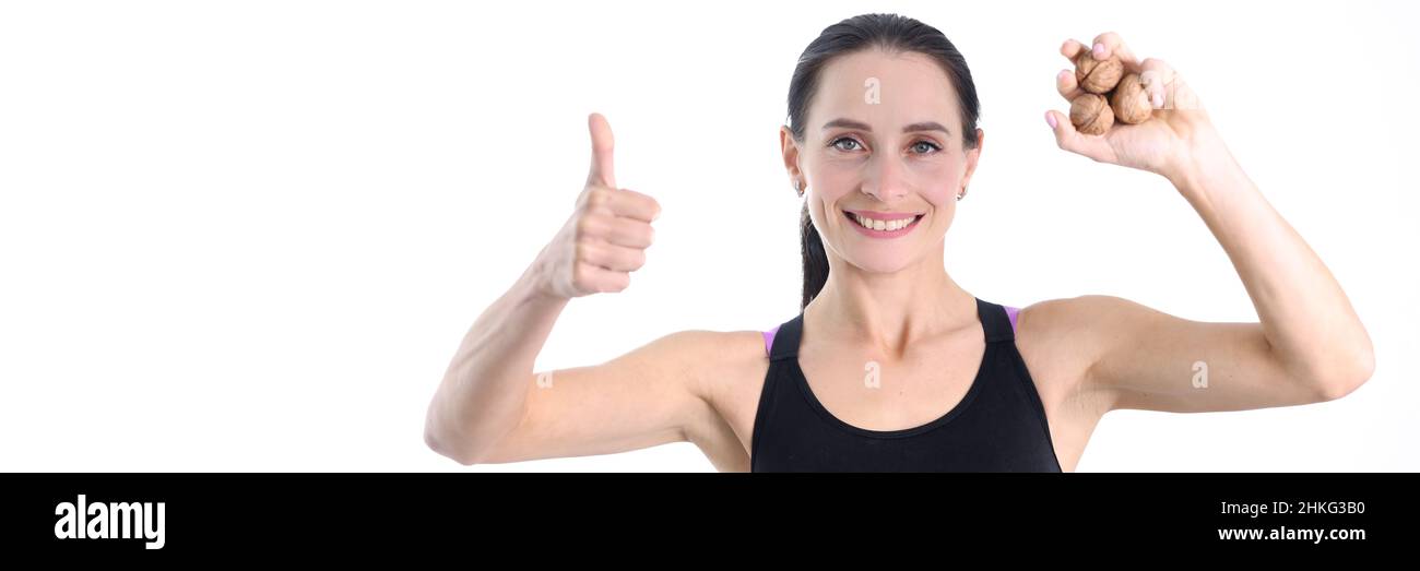 Junge, starke Frau, die Walnüsse in den Händen hält und eine gute Geste zeigt Stockfoto