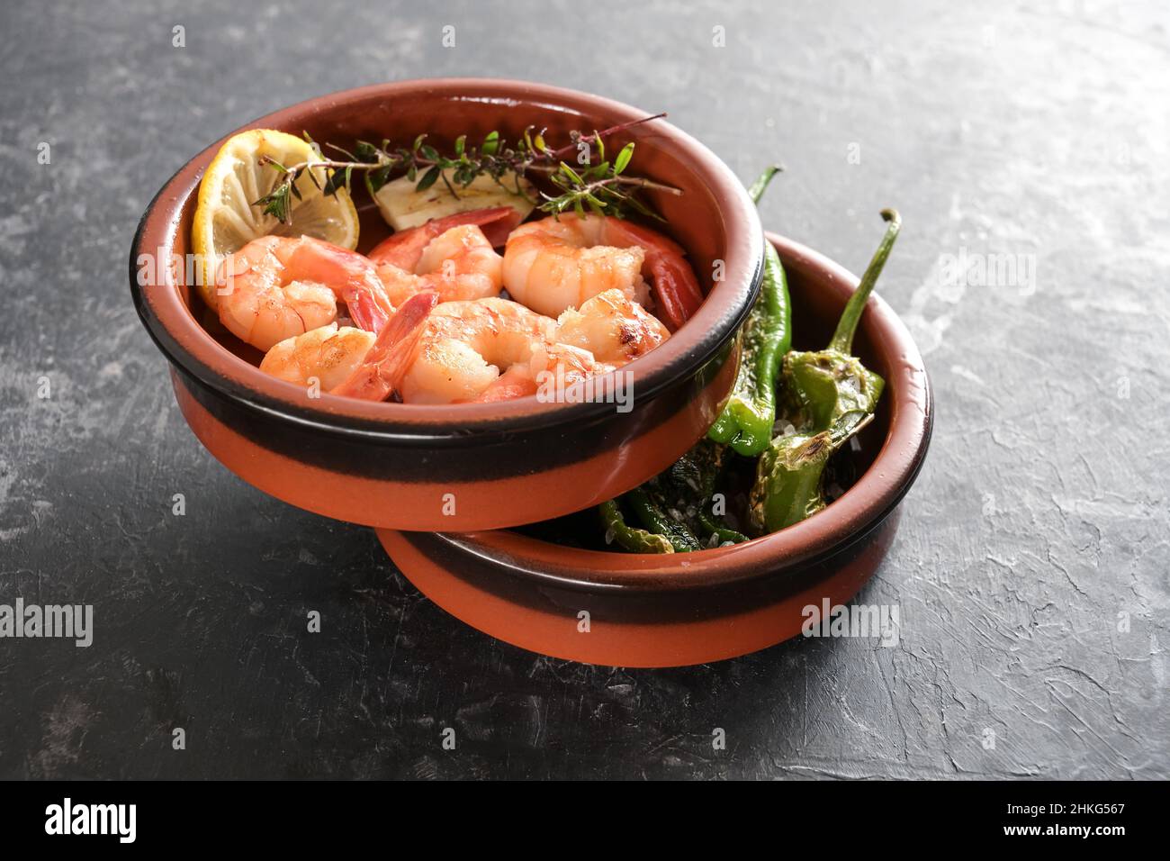 Gestapelte Tapa-Schalen mit Garnelen und gebratenen Pimientos oder padron-Paprika, spanische Vorspeise auf dunkelgrauem Schieferhintergrund, Kopierraum, ausgewählter Fokus, Stockfoto