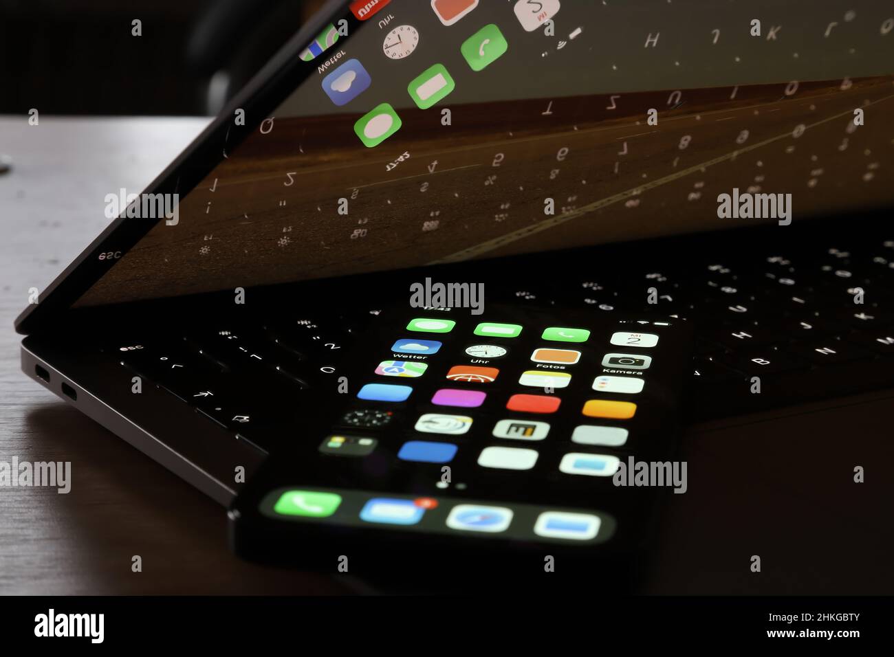 Smartphone auf einer beleuchteten Tastatur, die auf dem Monitor eines halb geschlossenen Laptops reflektiert wird Stockfoto