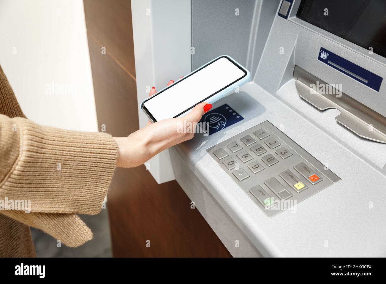 Weibliche Hand mit Mobiltelefon, das Geld vom geldautomaten abzieht, mit dem kontaktlosen NFC-wi-Fi-Bezahlsystem. Drahtlose Authentifizierung und Datenübertragung Stockfoto