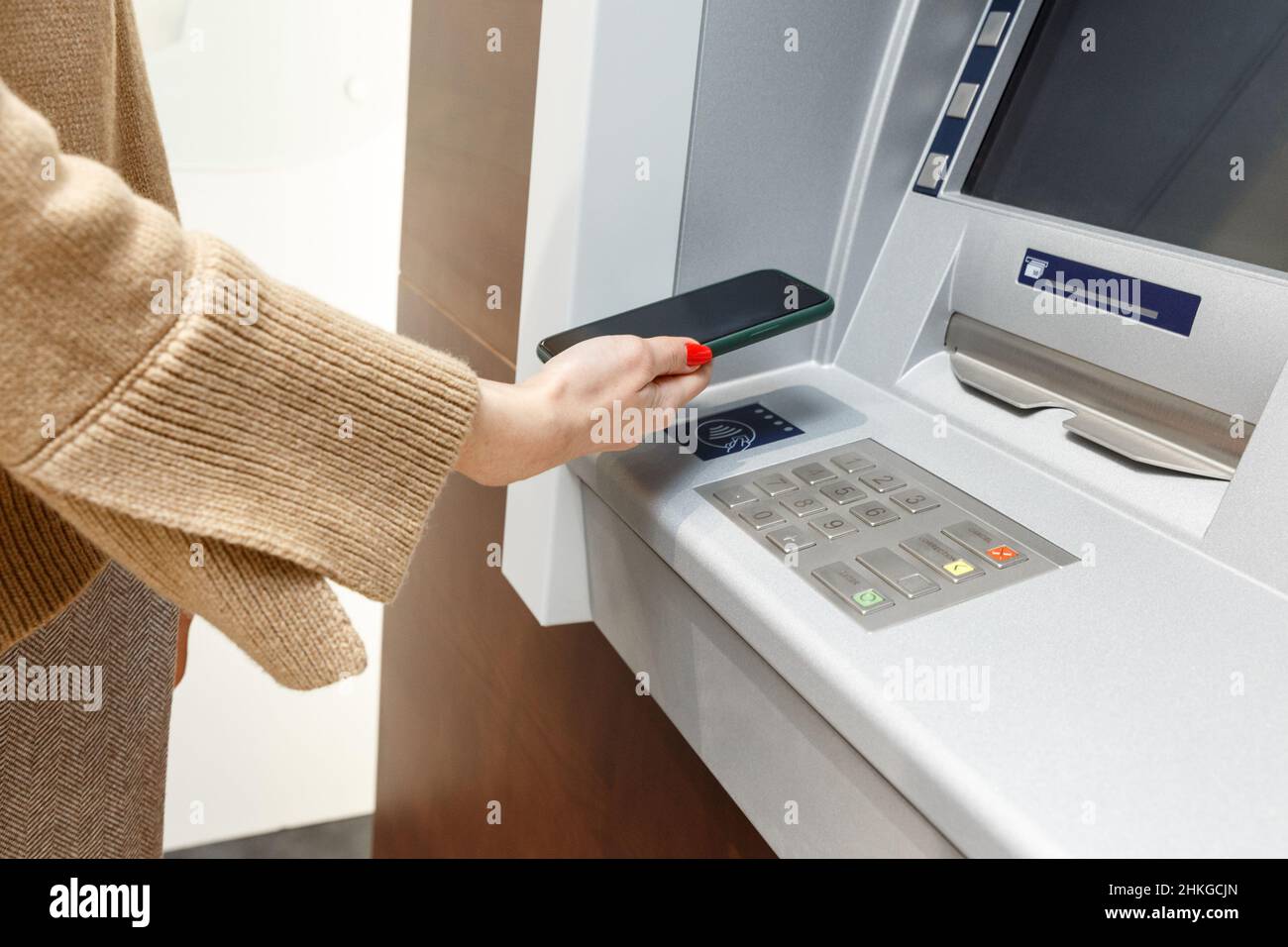 Weibliche Hand mit Mobiltelefon, das Geld vom geldautomaten abzieht, mit dem kontaktlosen NFC-wi-Fi-Bezahlsystem. Drahtlose Authentifizierung und Datenübertragung Stockfoto