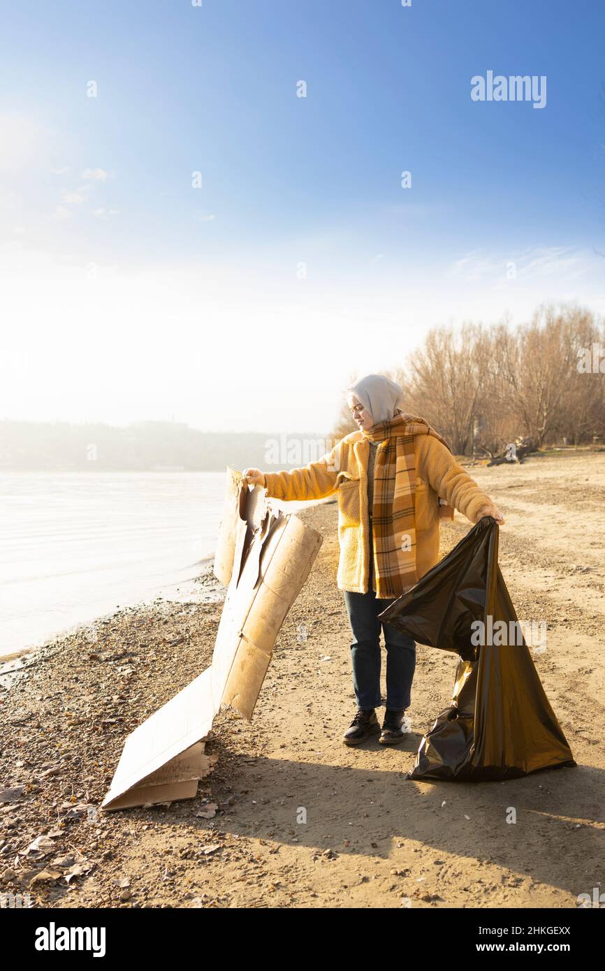 Eine junge Frau, die den Strand von Pappabfällen säubert Stockfoto