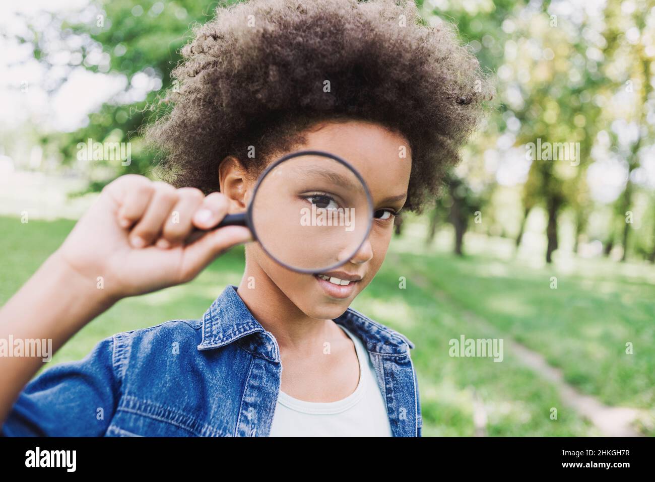 Lustige kleine Mädchen Blick durch eine Lupe. Nettes Kind im Freien Porträt. Menschen, Spaß, Kinder Lebensstil, Neugier, Wissenskonzept Stockfoto