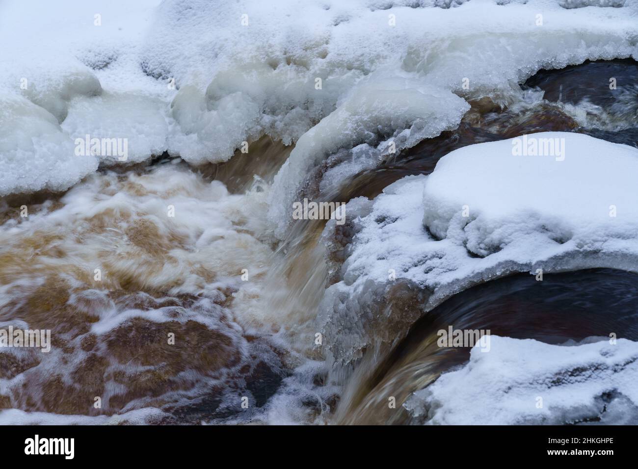 Eisfrei laufender Fluss im verschneiten Wald an einem düsteren kalten Wintertag Stockfoto