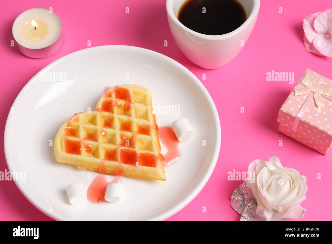 Nahaufnahme der hausgemachten herzförmigen Waffel mit Erdbeersirup, einer Tasse Kaffee und einer Geschenkbox. Romantisches Frühstück zum valentinstag Stockfoto
