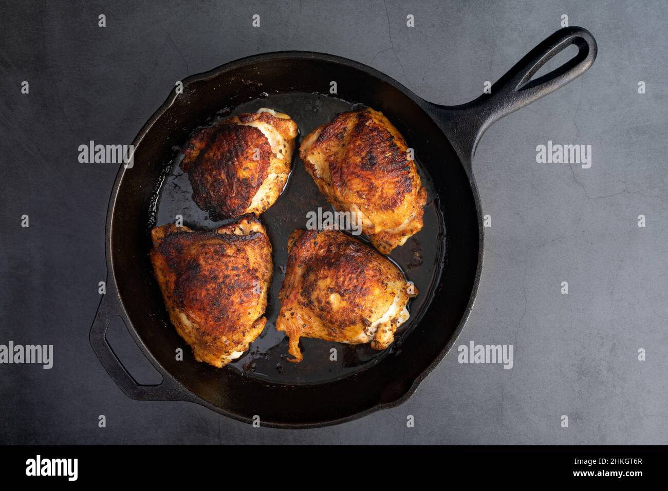 Ansicht von oben von gewürfelten Hühnerschenkeln in einer gusseisernen Pfanne: Gebratene, in Knochen eingewebte Hühnerschenkel, die in einer gusseisernen Bratpfanne gebraten werden Stockfoto