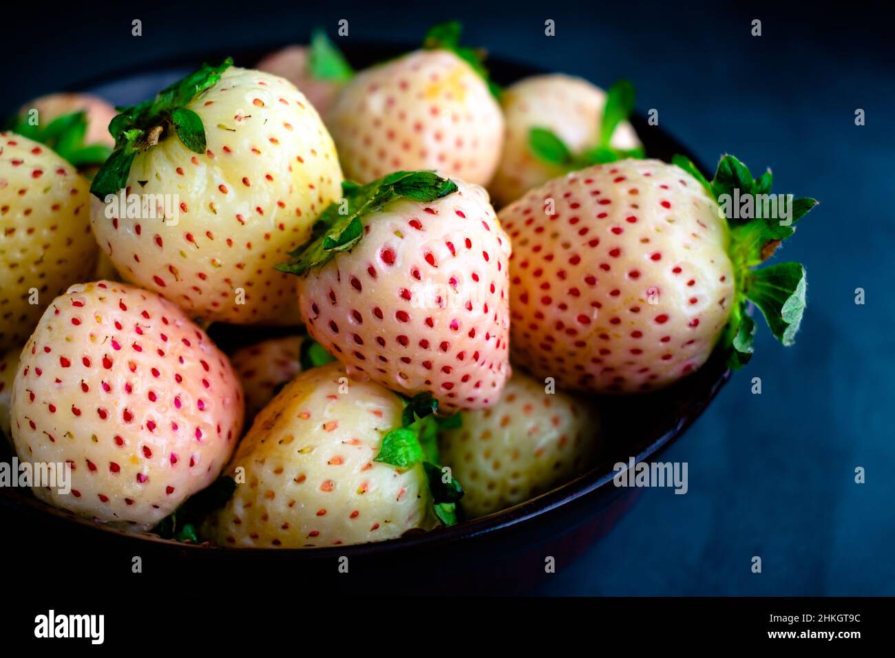 Frisch gewaschene Pineberries in einer Holzschüssel: Nahaufnahme von feuchten weißen Erdbeeren in einer dunklen Holzschüssel Stockfoto