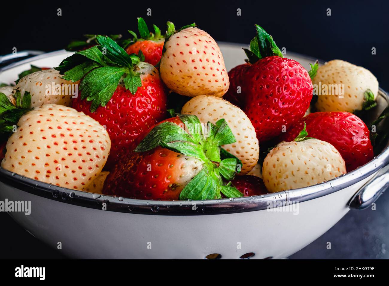 Mischung aus ganzen Pinelbeeren und Erdbeeren in einem Colander: Nahaufnahme von frisch gewaschenen roten und weißen Erdbeeren Stockfoto