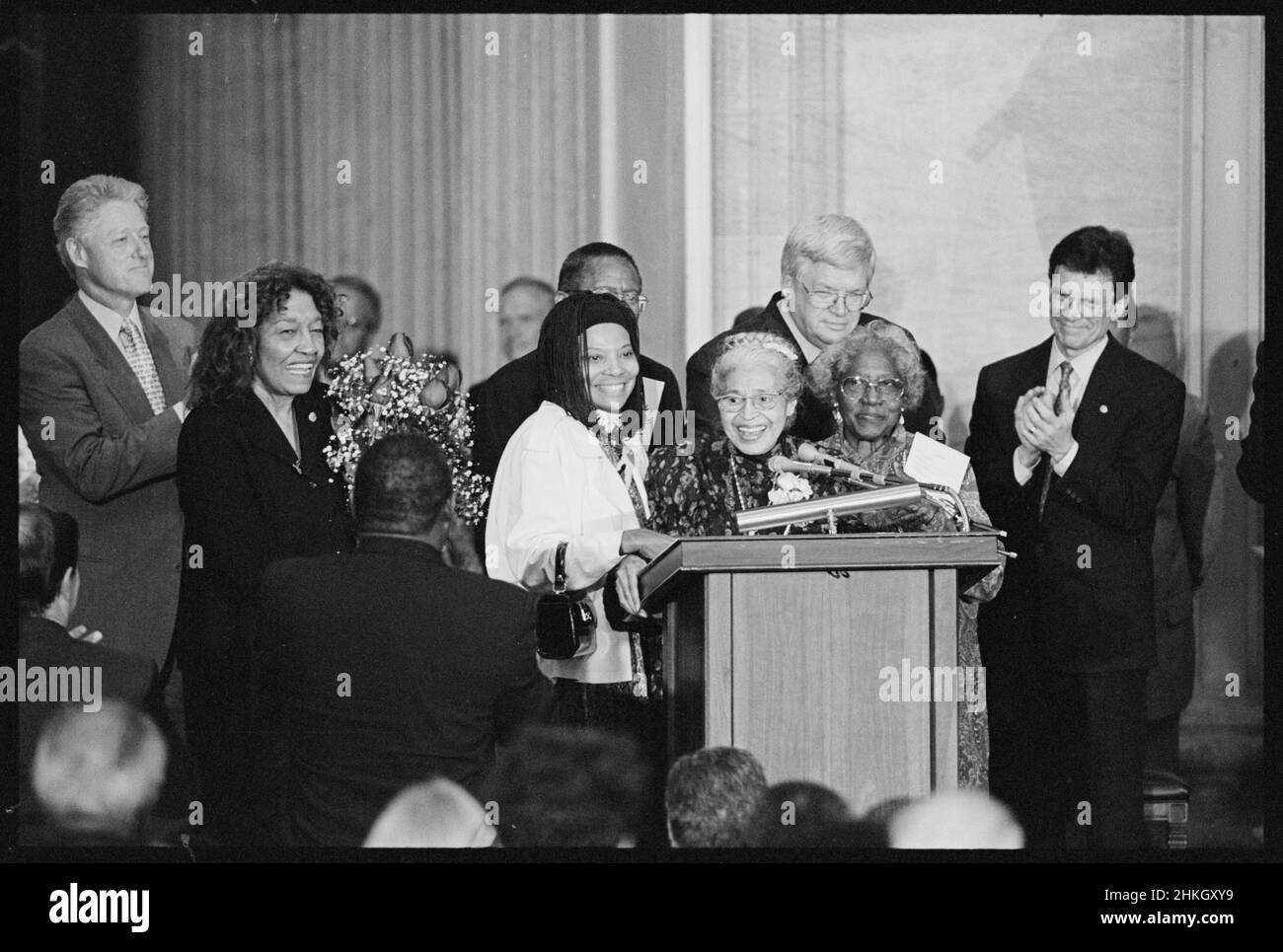 Rosa Parks bei der Verleihung der Goldmedaille im Kongress mit der Assistentin Elaine Steele (links) und der Bürgerrechtlerin Johnnie Carr (rechts) auf dem Podium; die Vertreterin Julia Carson, Präsidentin Clinton, Senator Tom Daschle, der Repräsentant Dennis Hastert und andere stehen neben ihr, Washington, DC, 6/15/1999. Stockfoto