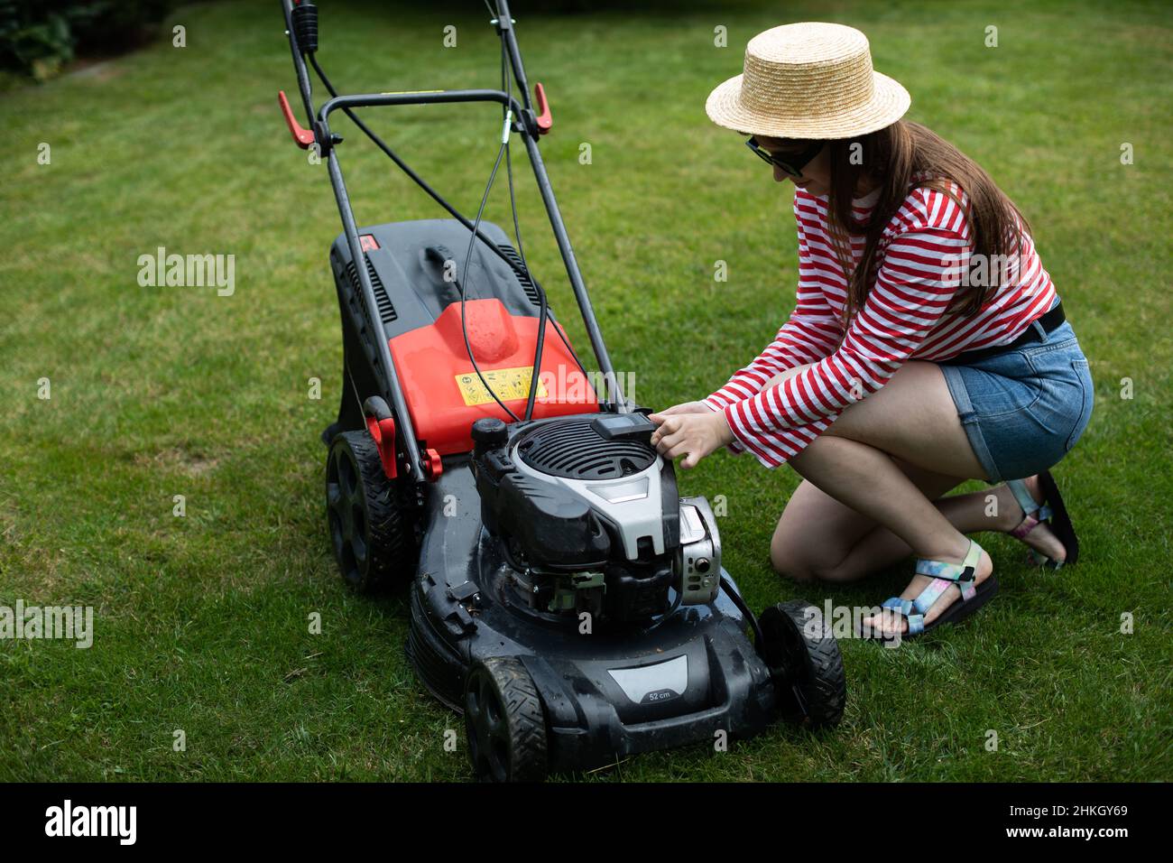 Ein Mädchen nimmt die Batterie aus einem Gartenmäher. Stockfoto