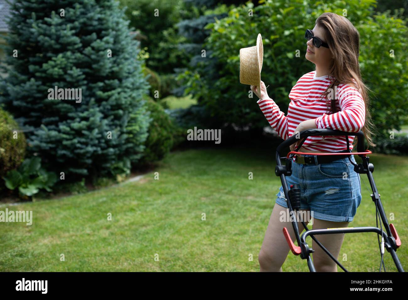Ein Mädchen fächtert sich mit einem Strohhut, während es das Gras schneidet. Stockfoto