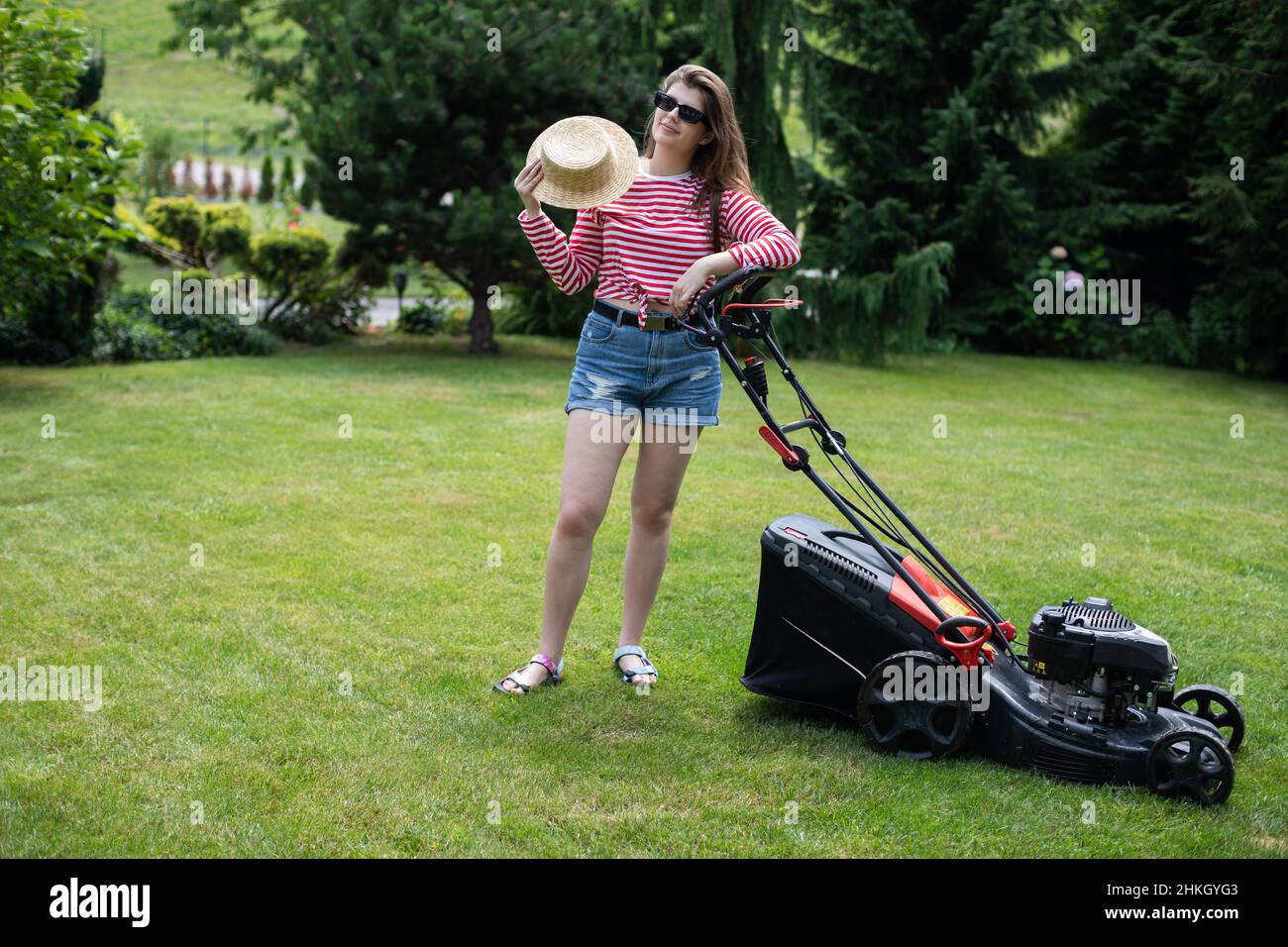 Ein Mädchen fächtert sich mit einem Strohhut, während es das Gras schneidet. Stockfoto