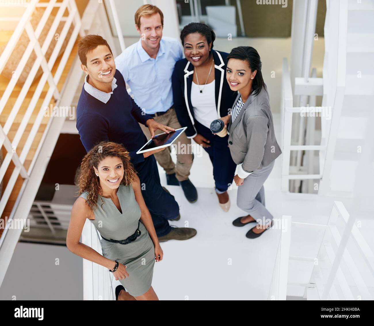 Erfolg, wir kommen für Sie. Porträt einer Gruppe lächelnder Mitarbeiter, die in einem modernen Büro auf einer Treppe stehen. Stockfoto