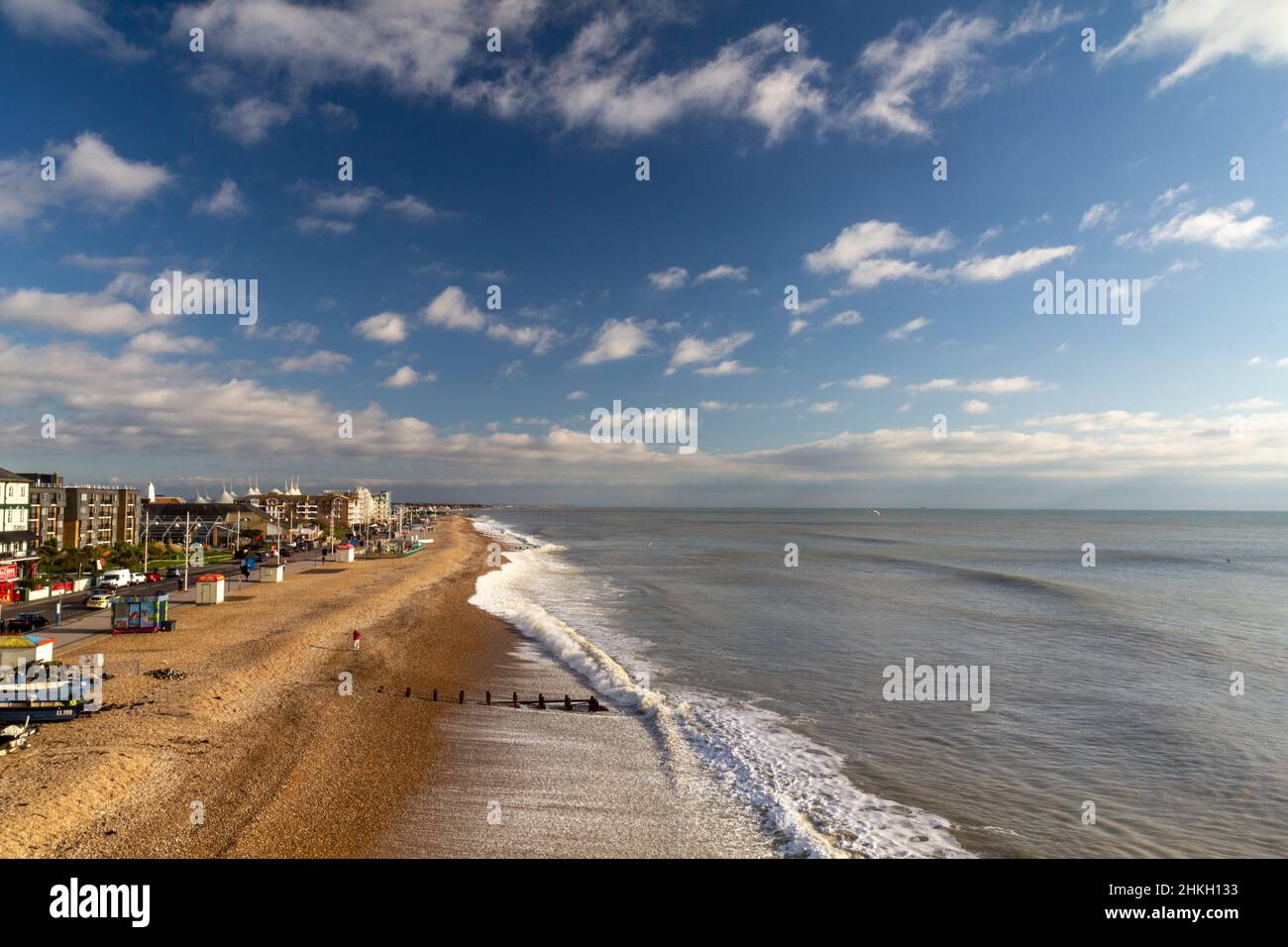 Bognor Regis Strand hoch oben Blick auf den Oststrand vom Pier nach Osten mit blauem Himmel und flauschigen Wolken mit Wellen, die auf die Küste krachen. Stockfoto