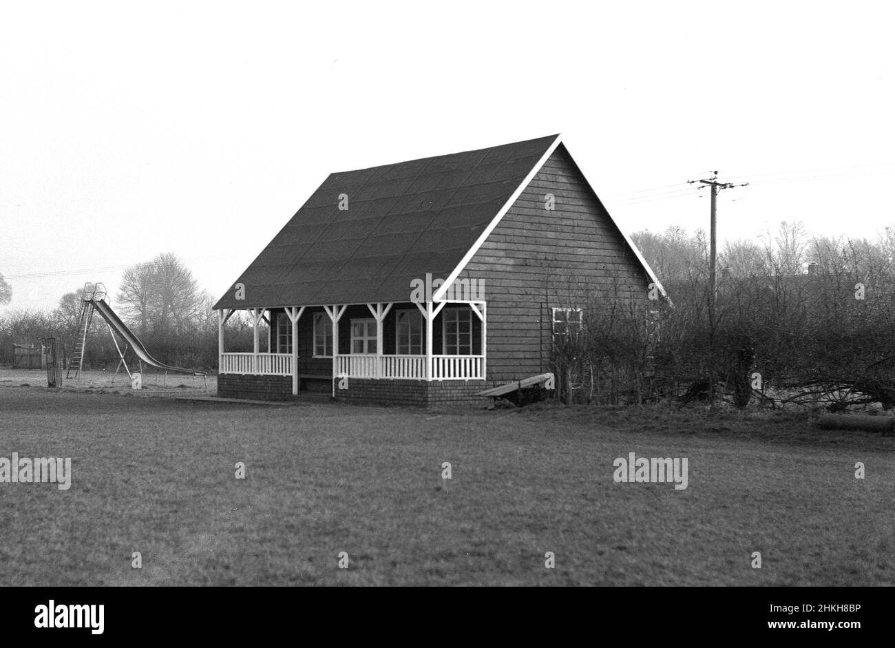 1950s, historisch, außen, Vorderansicht eines traditionellen Sportpavillons aus der Zeit, erbaut mit einem Holzrahmen auf einem Ziegelsockel und einem hoch abfallenden Dach. Architektonisch unverwechselbar mit einer überdachten Veranda oder Veranda an der Vorderseite, wurden diese Arten von einstöckigen Gebäuden am Rande von Sportplätzen zu dieser Zeit auf vielen Freizeit- und Sportplätzen in Großbritannien gesehen, die Umkleidekabinen für Mannschaftssportarten wie Cricket, Rugby und Fußball zur Verfügung stellten. Neben diesem neu errichteten Pavillon in Witney, Oxford, England, Großbritannien, gibt es einen Spielplatz für Kinder mit Medaillenrutsche. Stockfoto