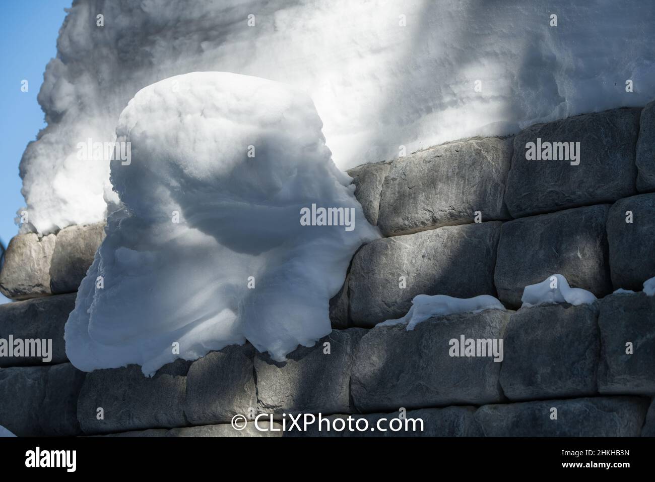 Schneeverwehung hängt an der von Menschen hergestellten Betonziegelwand rechteckige Ziegelsteine gestapelt außen Stützmauer mit schweren Schneelast horizontal Stockfoto