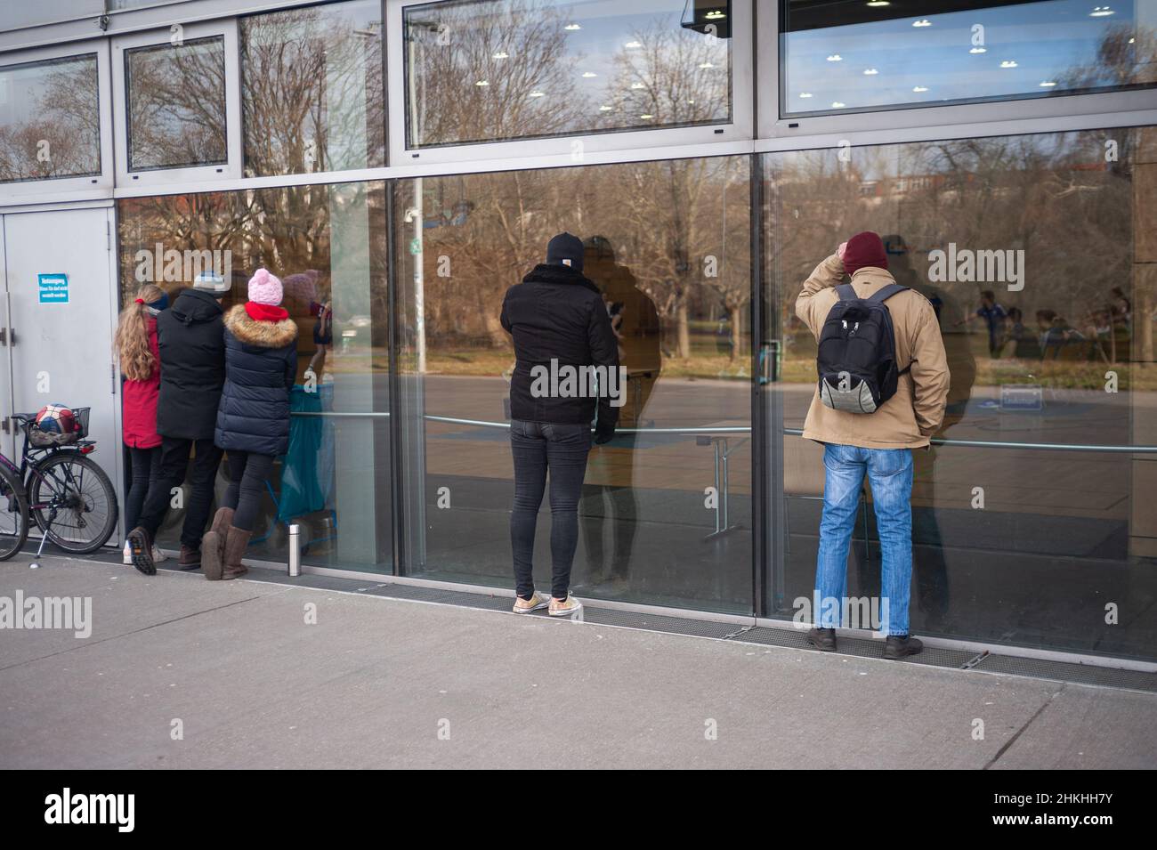 30.01.2022, Berlin, Deutschland, Europa - Zuschauer stehen vor einer Glasscheibe und schauen sich vor der Max-Schmeling-Halle ein Basketballspiel an. Stockfoto