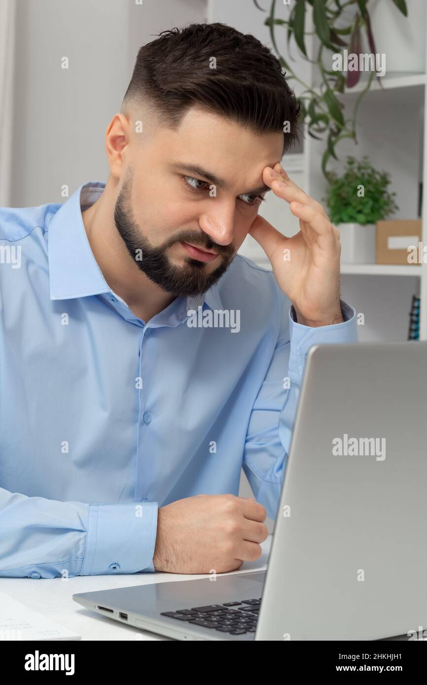 Schmerzen im Kopf eines müden Geschäftsmanns, der an einem Laptop arbeitet. Stockfoto