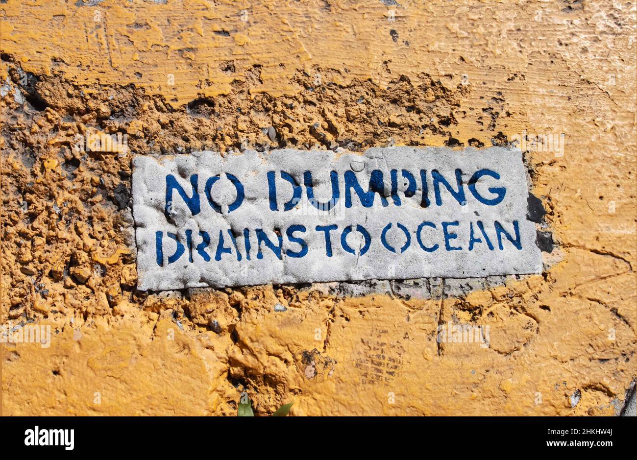 Kein Dumping – Schild „Drains to Ocean“ auf dem groben, gelb gestrichenen Gehweg Stockfoto