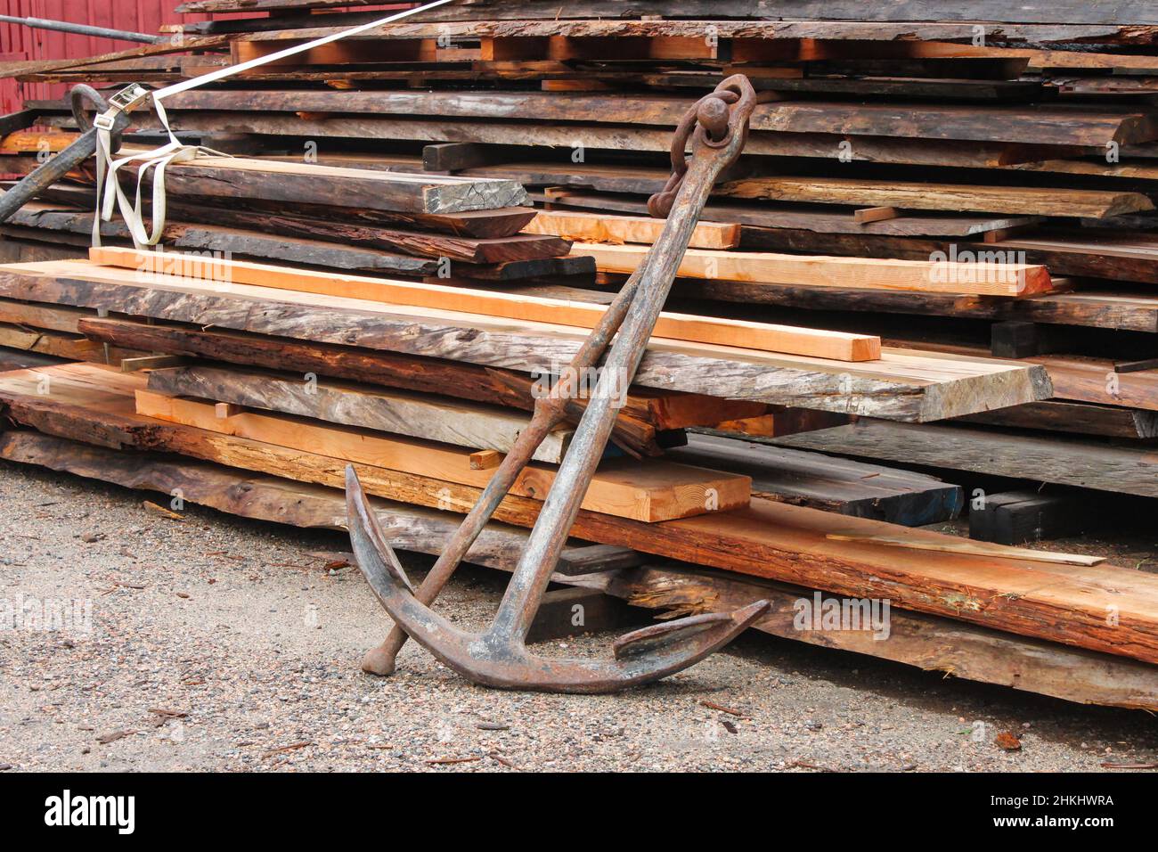 Alter verroster Anker, der sich an einen Holzhaufen lehnt, um Schiffe zu reparieren Stockfoto