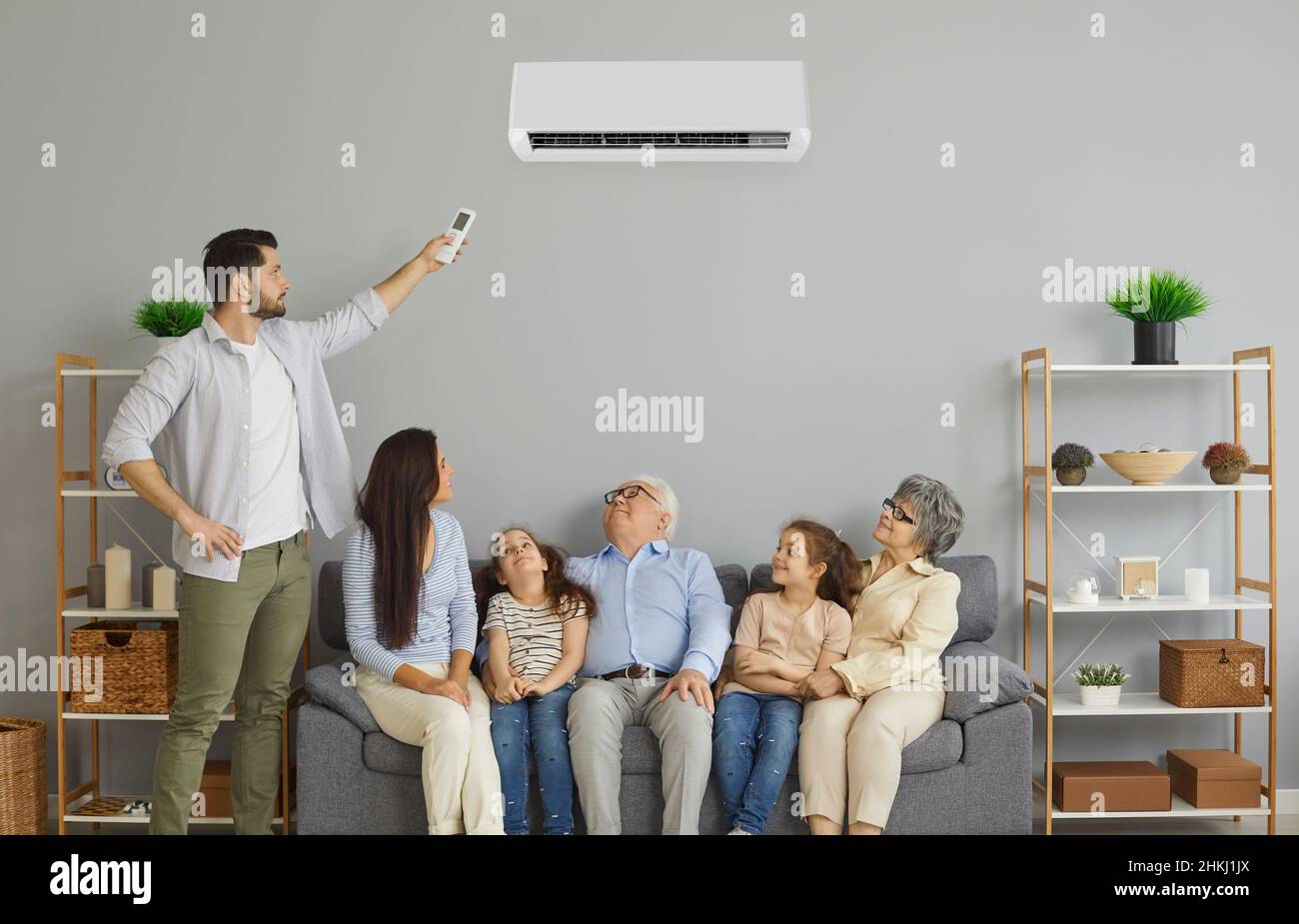 Glückliche Familie, die auf dem Sofa im Wohnzimmer mit einer modernen Klimaanlage sitzt Stockfoto