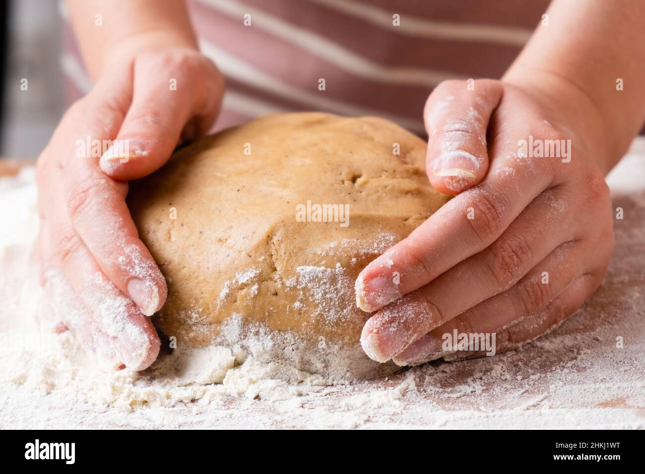 Draufsicht auf Frauenhände, die den Teig für Brötchen, Kuchen, Kekse oder Gebäck auf dem Holzschreibtisch kneten. Prozess der hausgemachten Küche. Stockfoto