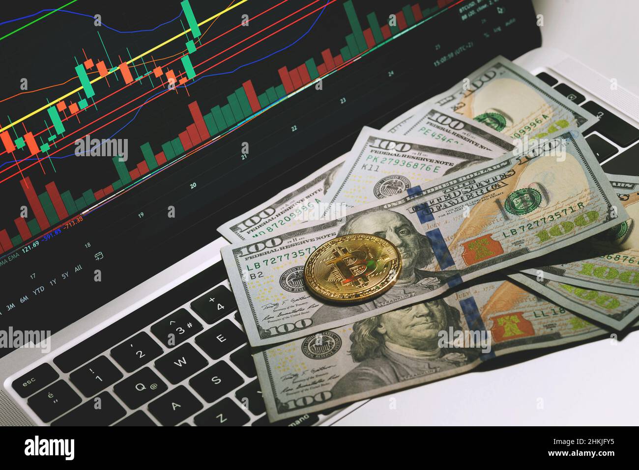 Nahaufnahme von 100-Dollar-Banknoten und einer Bitcoin-Münze auf ihnen und auf einem Notebook-Computer mit Börsenanzeigen auf dem Bildschirm. Stockfoto