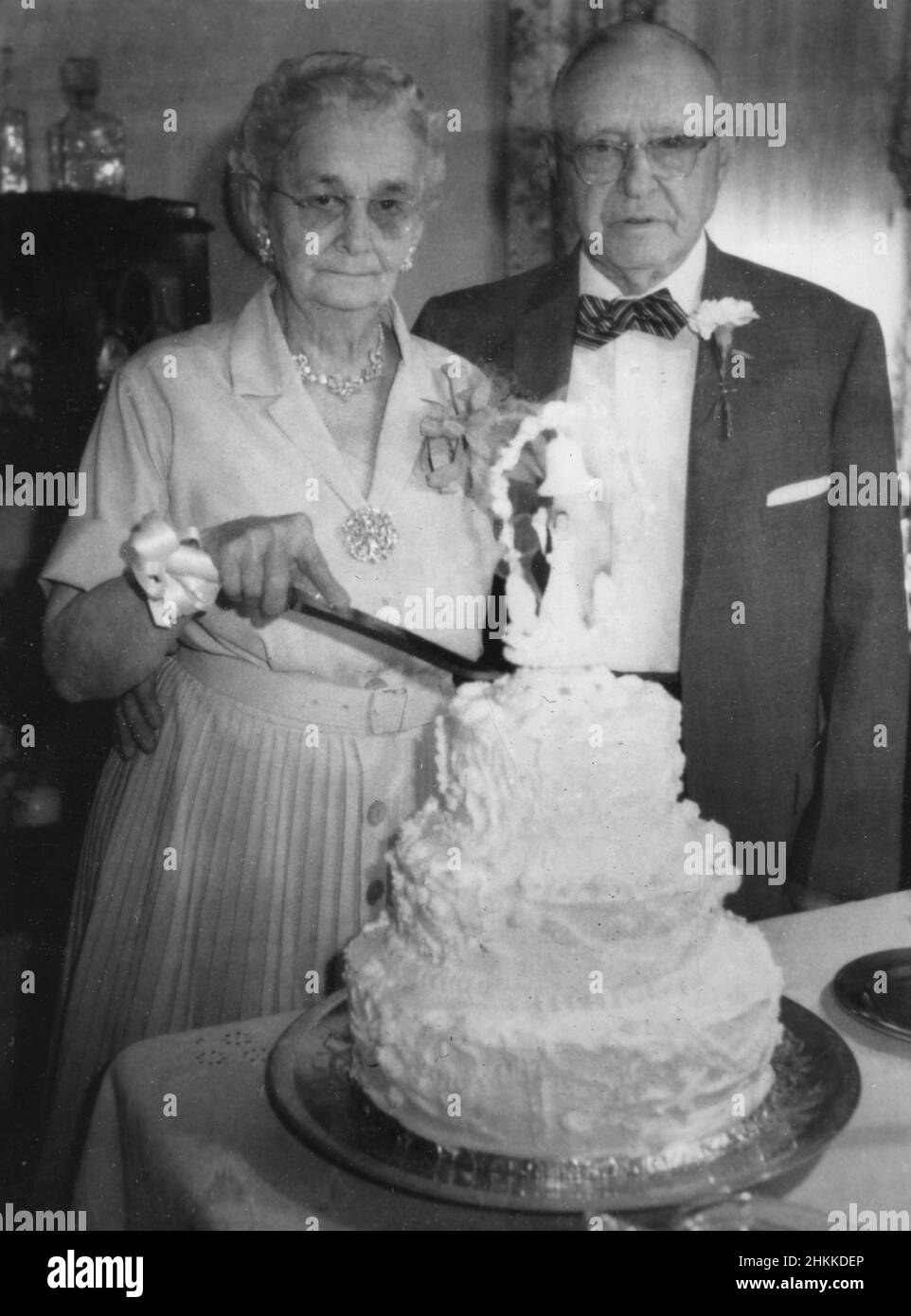 Ein Seniorenpaar scheint unemotional zu sein, wenn es darum geht, ihren Golden Anniversary Kuchen zu schneiden, Ca. 1958. Stockfoto