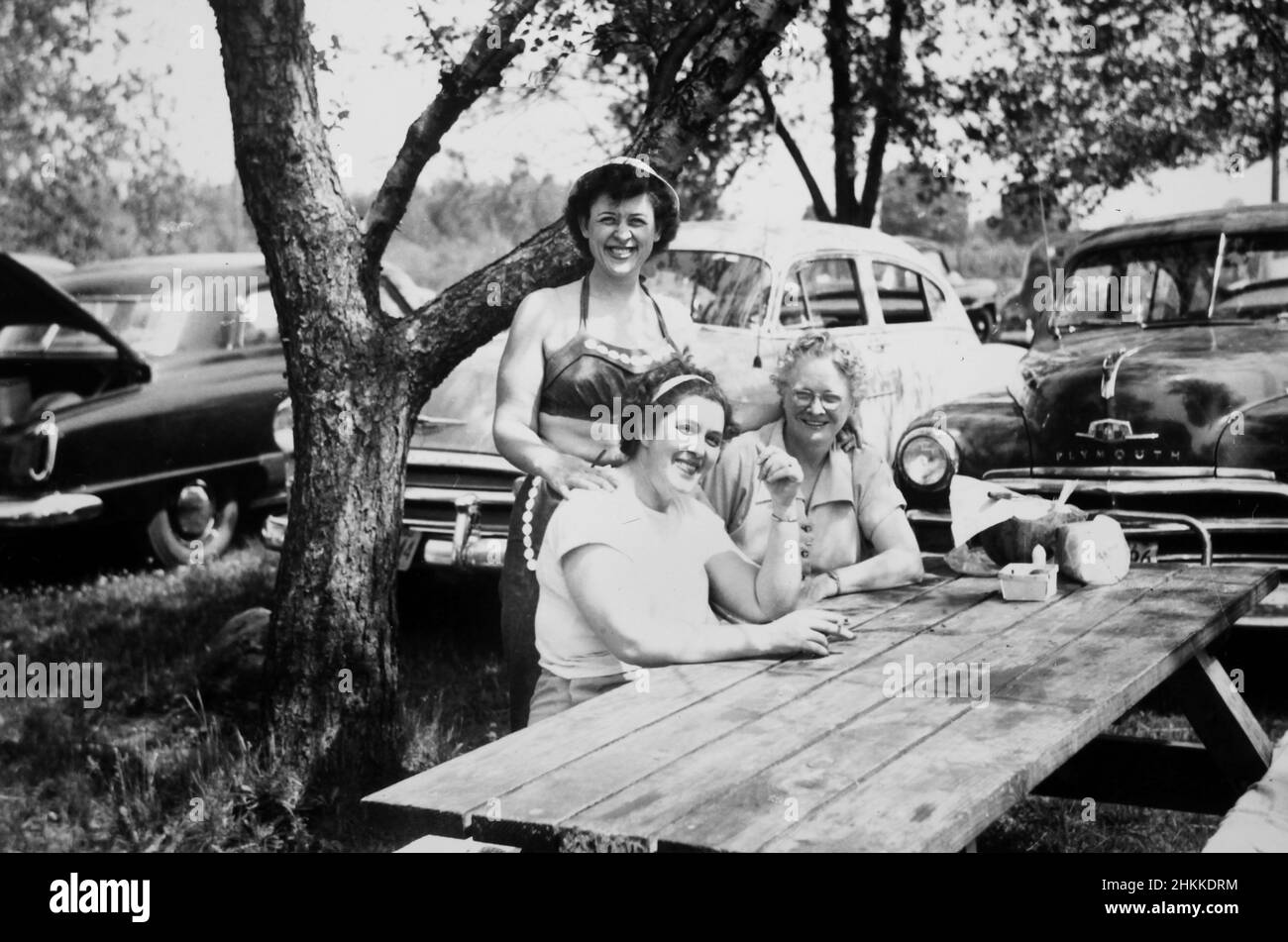 Drei Frauen entspannen sich zusammen an einem Picknicktisch neben dem Parkplatz, ca. 1950. Stockfoto