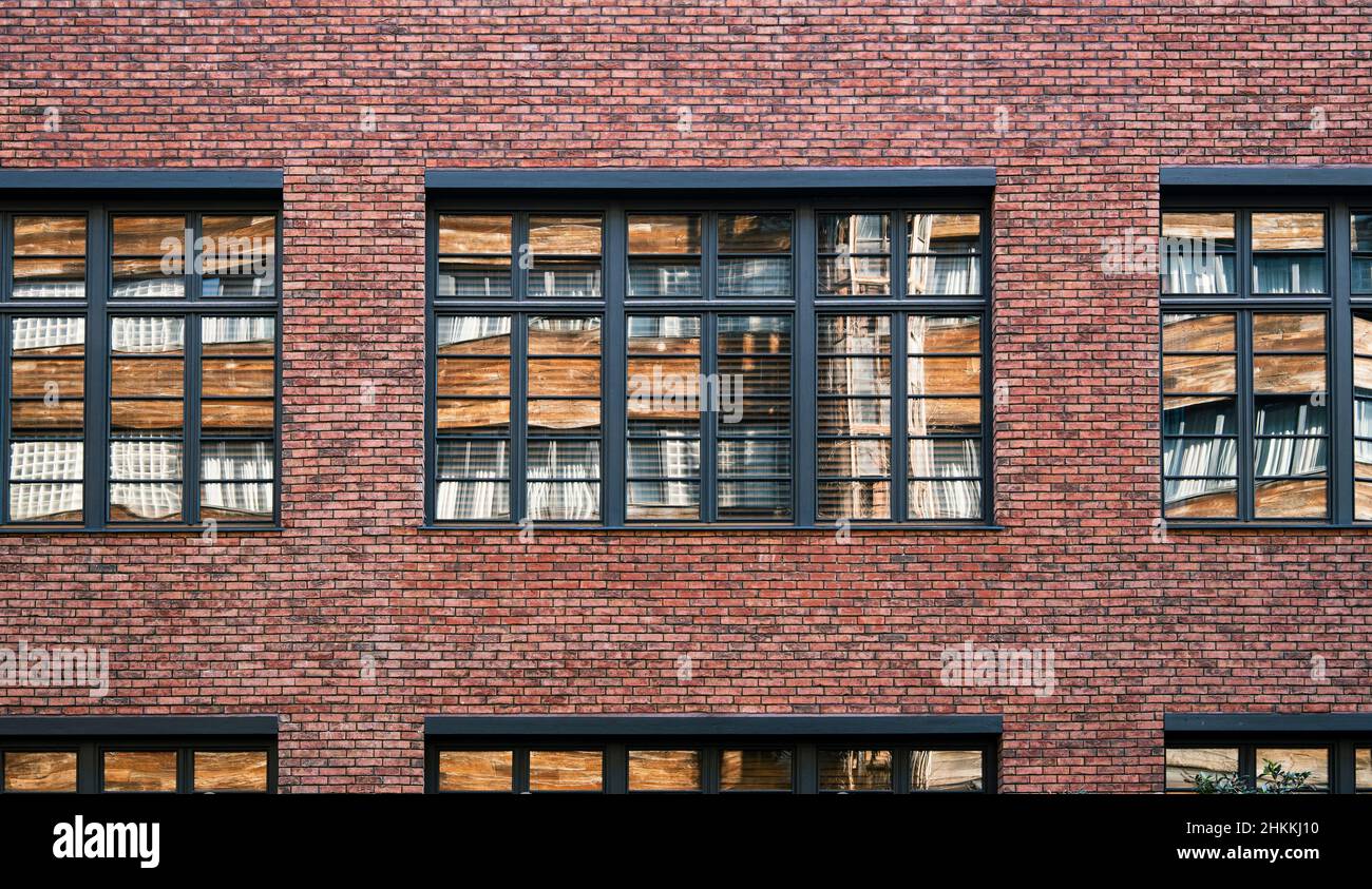Fassadenwand eines Backsteingebäudes mit Fenstern. Die gegenüberliegende Wand spiegelt sich in der Fensterscheibe wider. Glatte Reihen von altem Mauerwerk. Hintergrundbild, Screensave Stockfoto